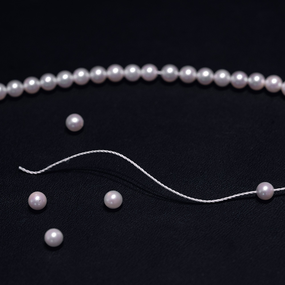 Weiße Perlenkette – Schmuckfoto mit losem Fadenende und vier einzelnen Perlen auf dunklem Untergrund