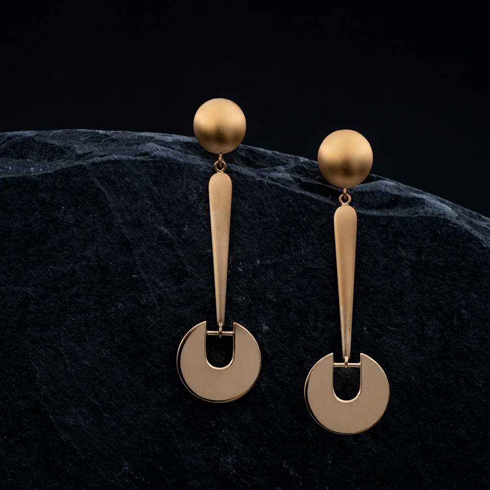 Elegante goldene Ohrringe mit geometrischem Design – runde Stecker und längliche Anhänger mit kreisförmigem Element auf dunklem Stein-Hintergrund.